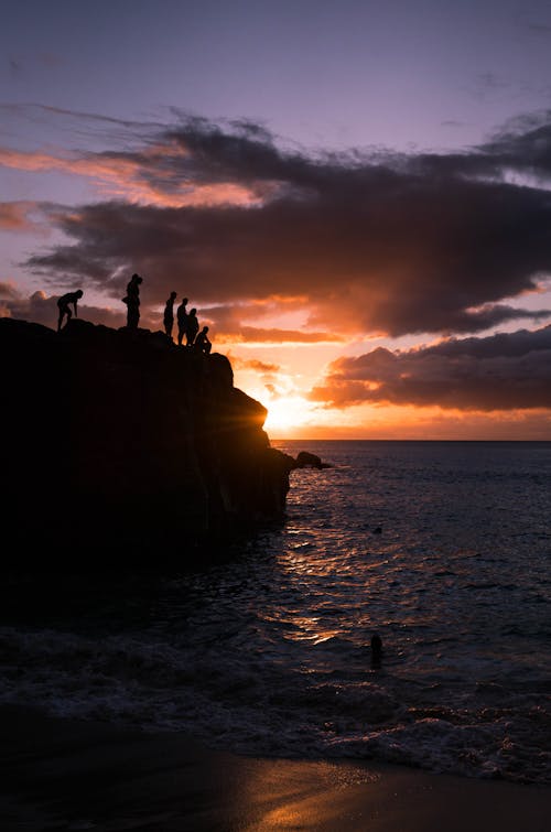 Anonymous people enjoying sunset over sea from rocky cliff