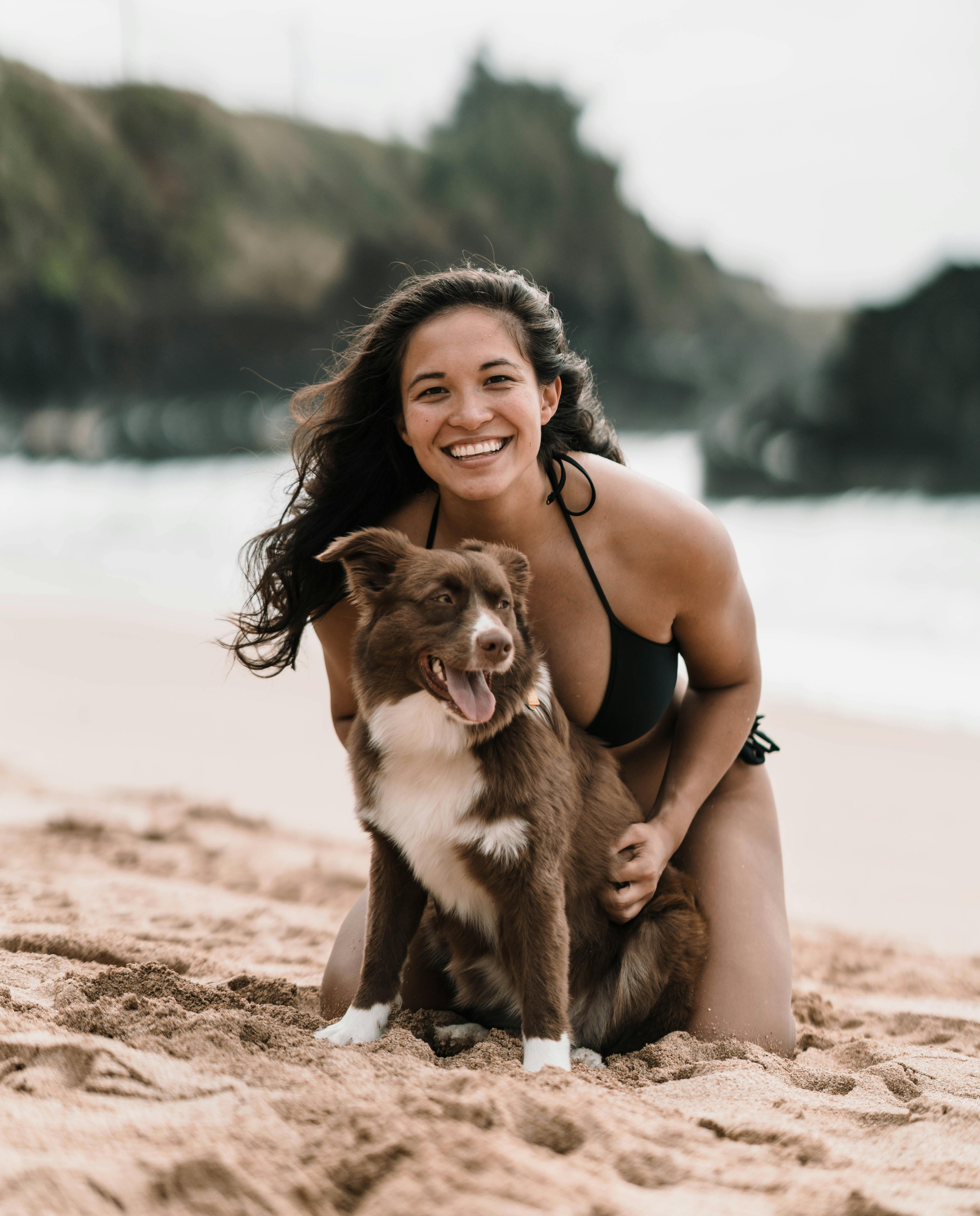 Joyful young female with purebred dog having fun on sandy seashore