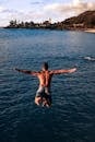 Back view of unrecognizable shirtless muscular male traveler jumping into blue sea water with outstretched arms on sunny day