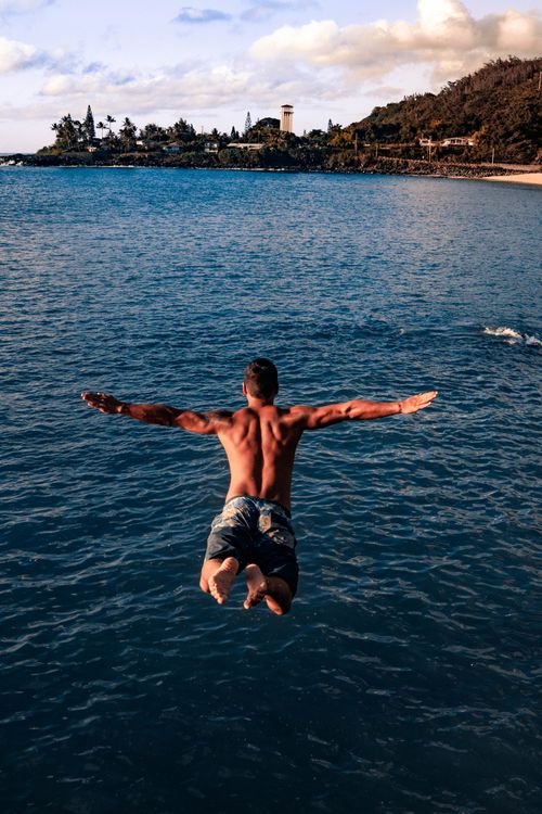 Free Back view of unrecognizable shirtless muscular male traveler jumping into blue sea water with outstretched arms on sunny day Stock Photo