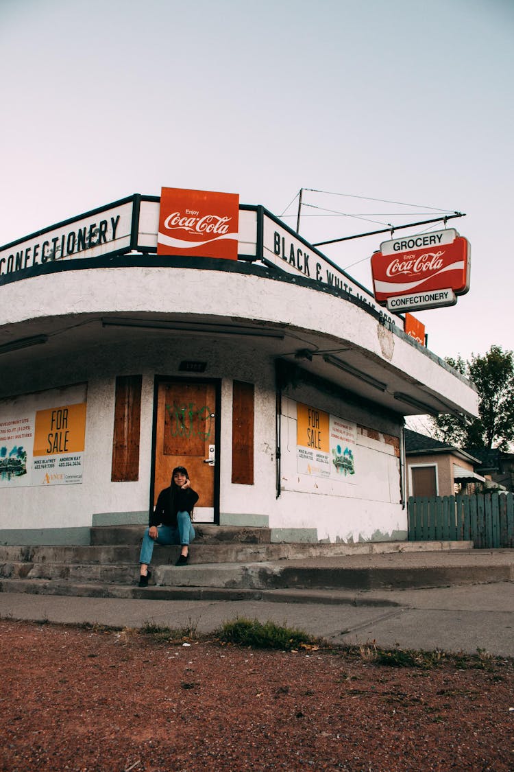 A Woman In Black Sweater Sitting On A Concrete Stairs In Front Of The Grocery Store