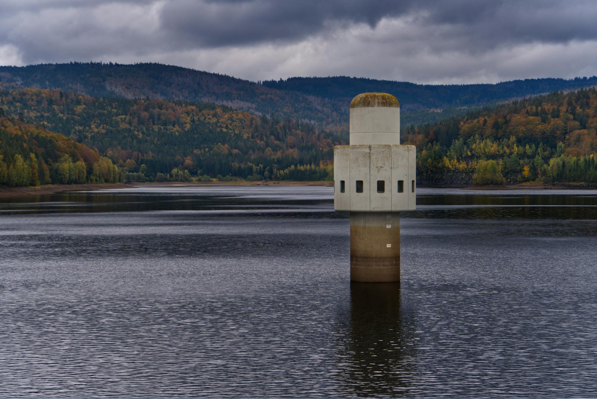 A concrete intake tower stands in a tranquil reservoir surrounded by lush autumn forests.