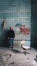 Anonymous depressed male standing near weathered graffiti wall and chair in old damaged house