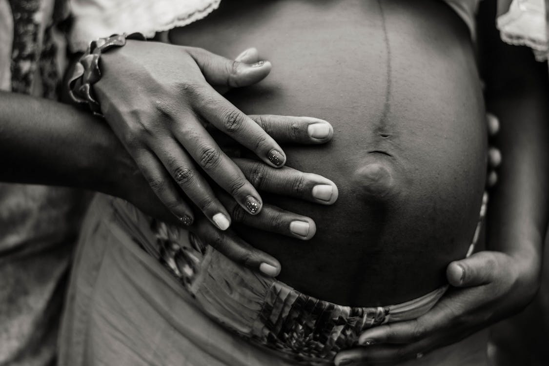 Free Black and white of unrecognizable pregnant African American female in embrace with husband holding hands on belly Stock Photo