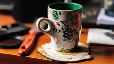 Cup with green and red ornaments on wooden table in daytime on blurred background