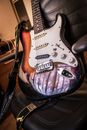 Classic electric guitar with strings and belt on black leather seat at home