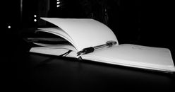 Opened notebook with black pen and bookmark on black surface