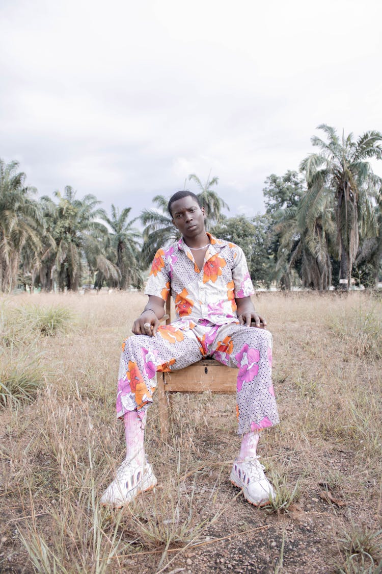 Black Man Sitting On Chair In Field