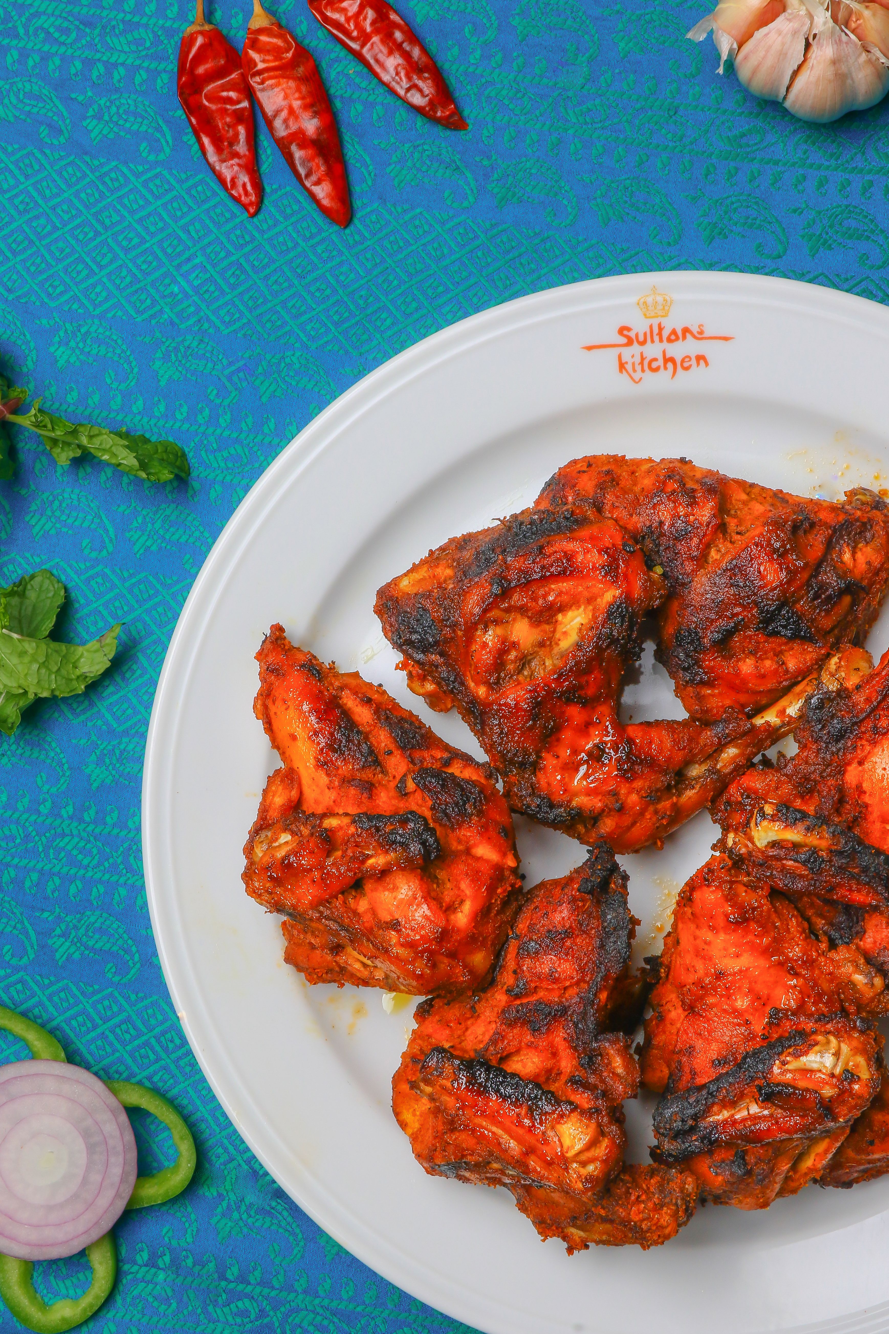 Golden-brown tandoori chicken wings with charred edges, drizzled with bright red chili oil and garnished with fresh cilantro and thin red onion slices on a white plate