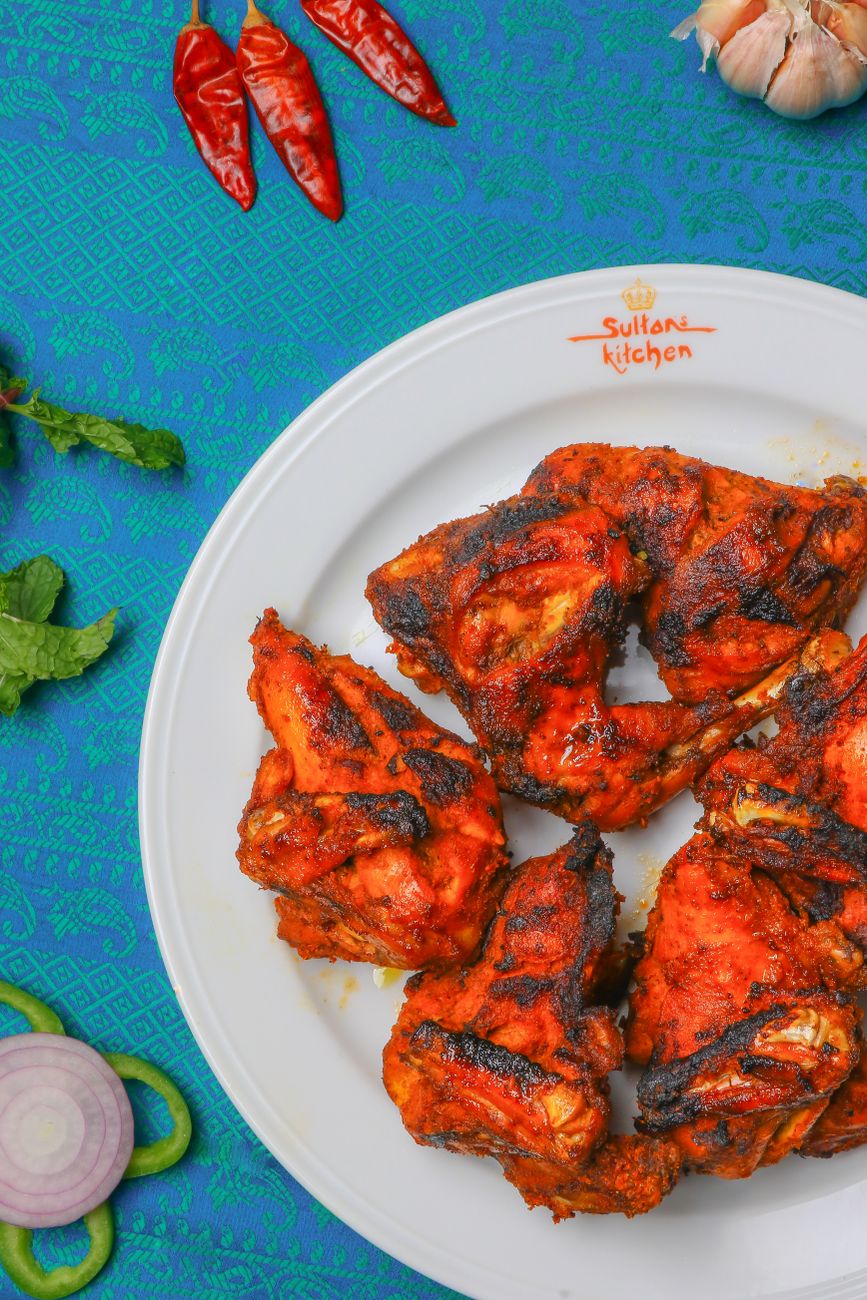 Golden-brown tandoori chicken wings with charred edges, drizzled with bright red chili oil and garnished with fresh cilantro and thin red onion slices on a white plate