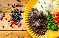 Top view arrangement of tasty black bean stew served on yellow plate with rice and couscous topped with cut tomatoes and parsley