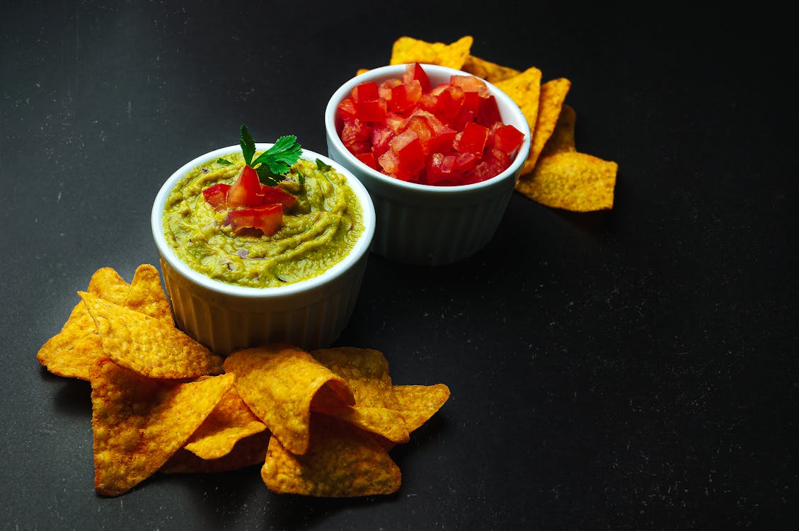 Crispy nachos on black table near guacamole and cut tomatoes