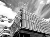 一张黑白照片中，一座现代玻璃建筑以低角度呈现，天空布满戏剧性的云层