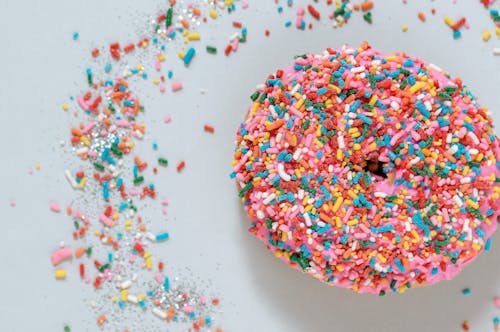 Free Overhead composition of freshly baked donut topped with multicolored sweet sprinkles and placed on light blue table Stock Photo