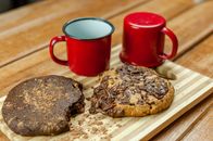 Delicious chocolate cookies near tin cups prepared for breakfast on wooden striped board on blurred background of table