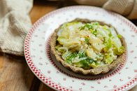 From above of tasty appetizing salad served in crusty tartlet on dish placed on wooden table