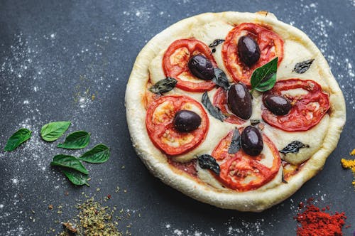 Flat lay of pizza of thick dough with cheese decorated with green leaves and bright condiment