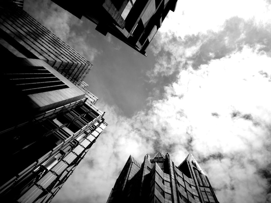 Low angle view of towering skyscrapers against a cloudy sky in monochrome depicting urban architecture.