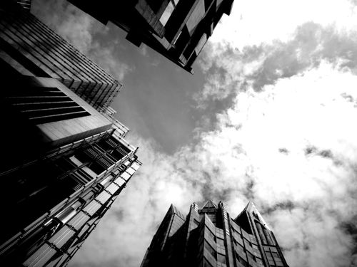 Free Low angle view of towering skyscrapers against a cloudy sky in monochrome depicting urban architecture. Stock Photo