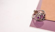 From above of silver ring with bright jewels placed on purple surface with scattered paper