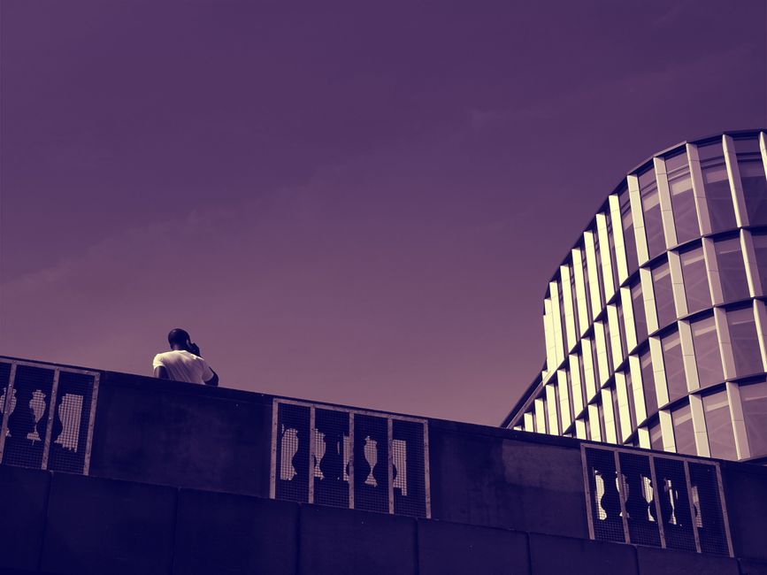 Una persona está de pie junto a un edificio contemporáneo, capturando la soledad en la arquitectura urbana.