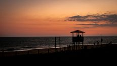Silhouette of observation post with triangular roof on shore of dark blue silent endless sea under vivid sunset in evening