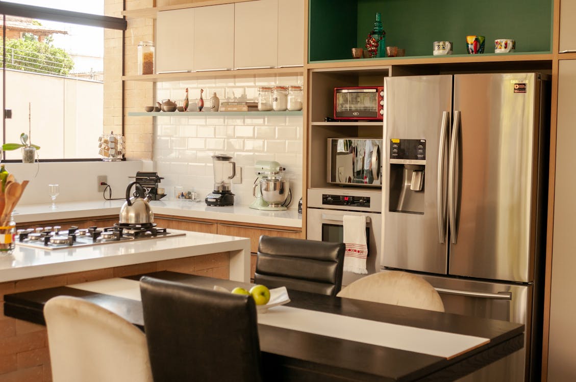 Wooden table with chairs placed in modern kitchen near stylish stainless steel refrigerator and oven in daylight