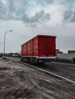 Large heavy motor vehicle driving on roadway while transporting goods along village in cloudy day