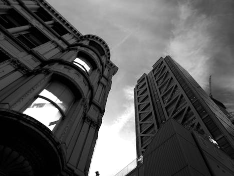 黑白低角度视角下，历史与现代建筑在多云的天空映衬下形成鲜明对比
