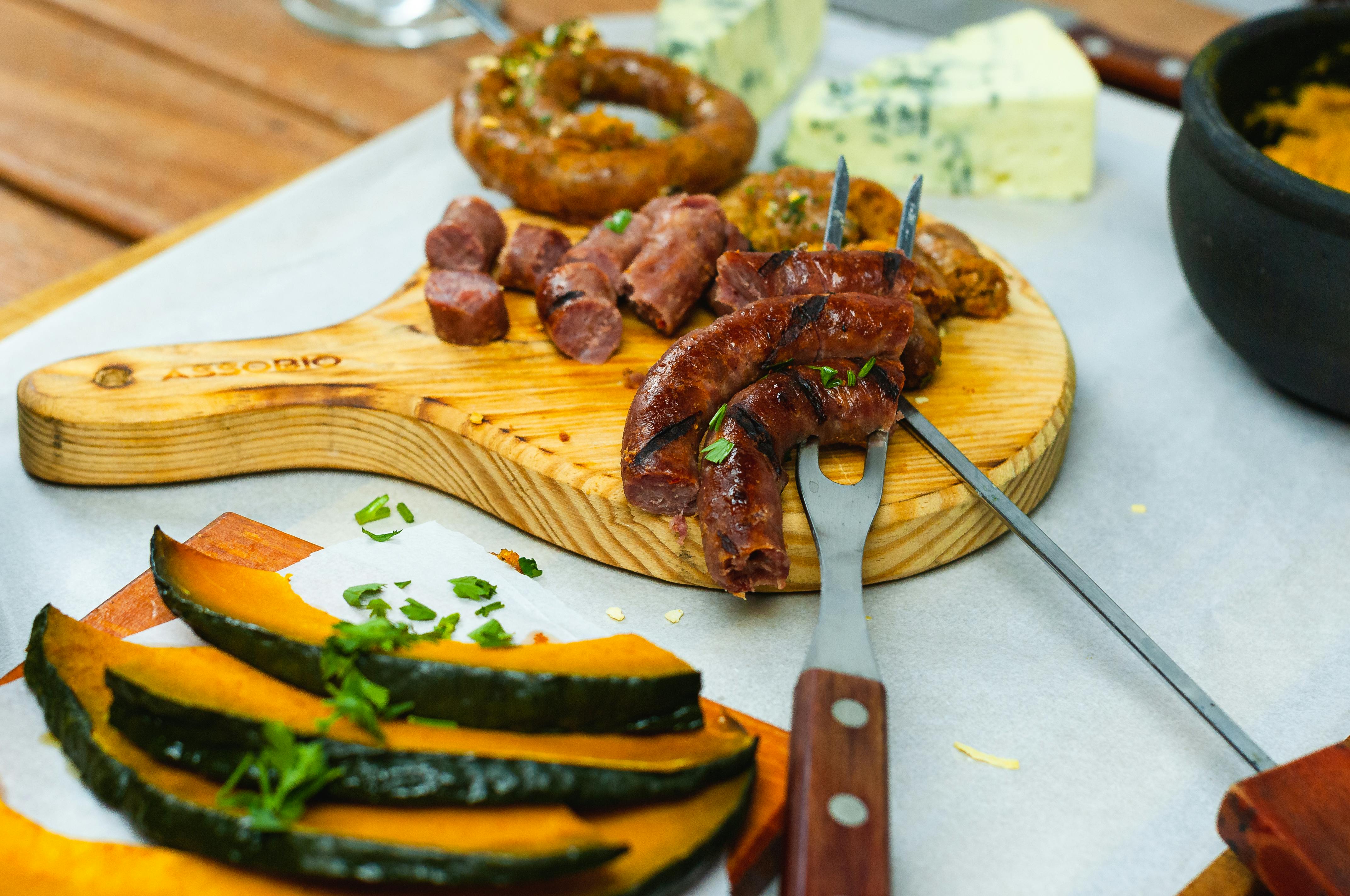 Composition of appetizing cut sausage served on wooden board with boiled pumpkin and blue cheese