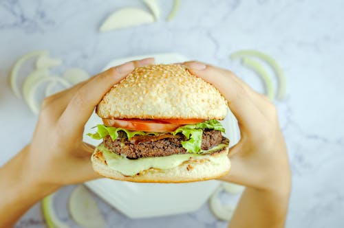 Anonymous person eating hamburger with cutlet and fresh vegetables