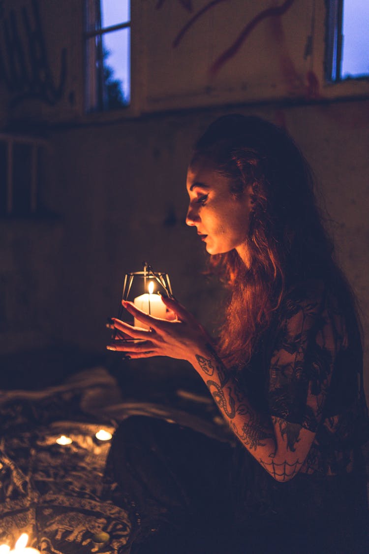 Tattooed Woman Praying With Candle In Darkness