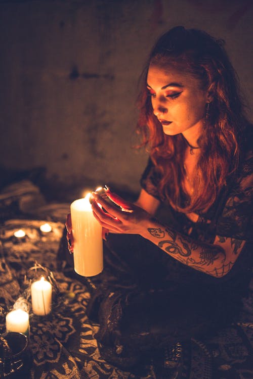 Calm dark female sitting in grunge room and burning candles doing spooky cult ritual