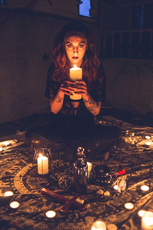 Free Creepy woman holding candle and looking at camera sitting in warm light prepare for ritual Stock Photo