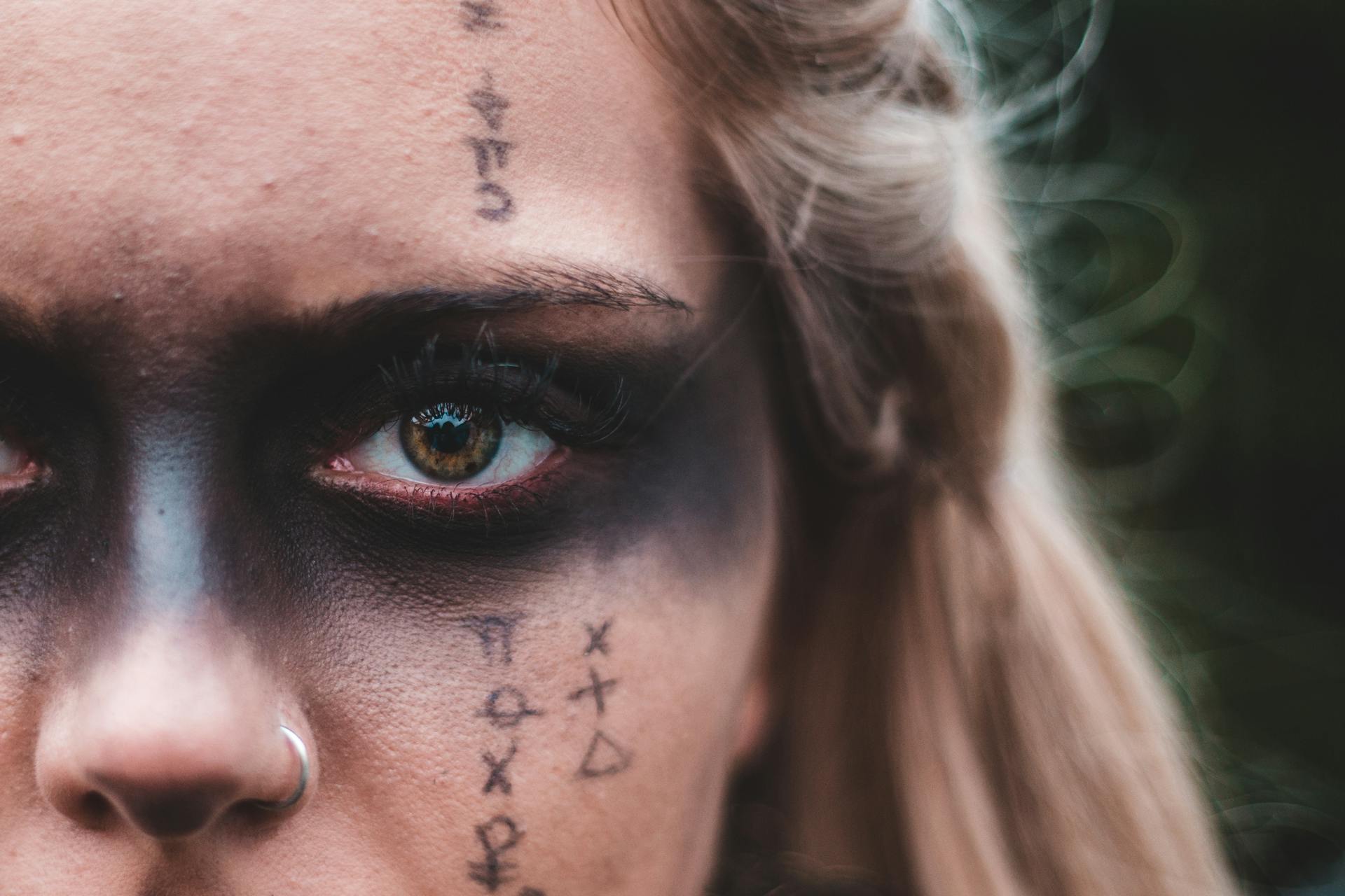 Closeup crop blond with black painted mask on eyes and symbols on skin looking at camera