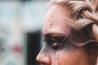 Crop side view of blond woman with black mask makeup and symbols on face looking away