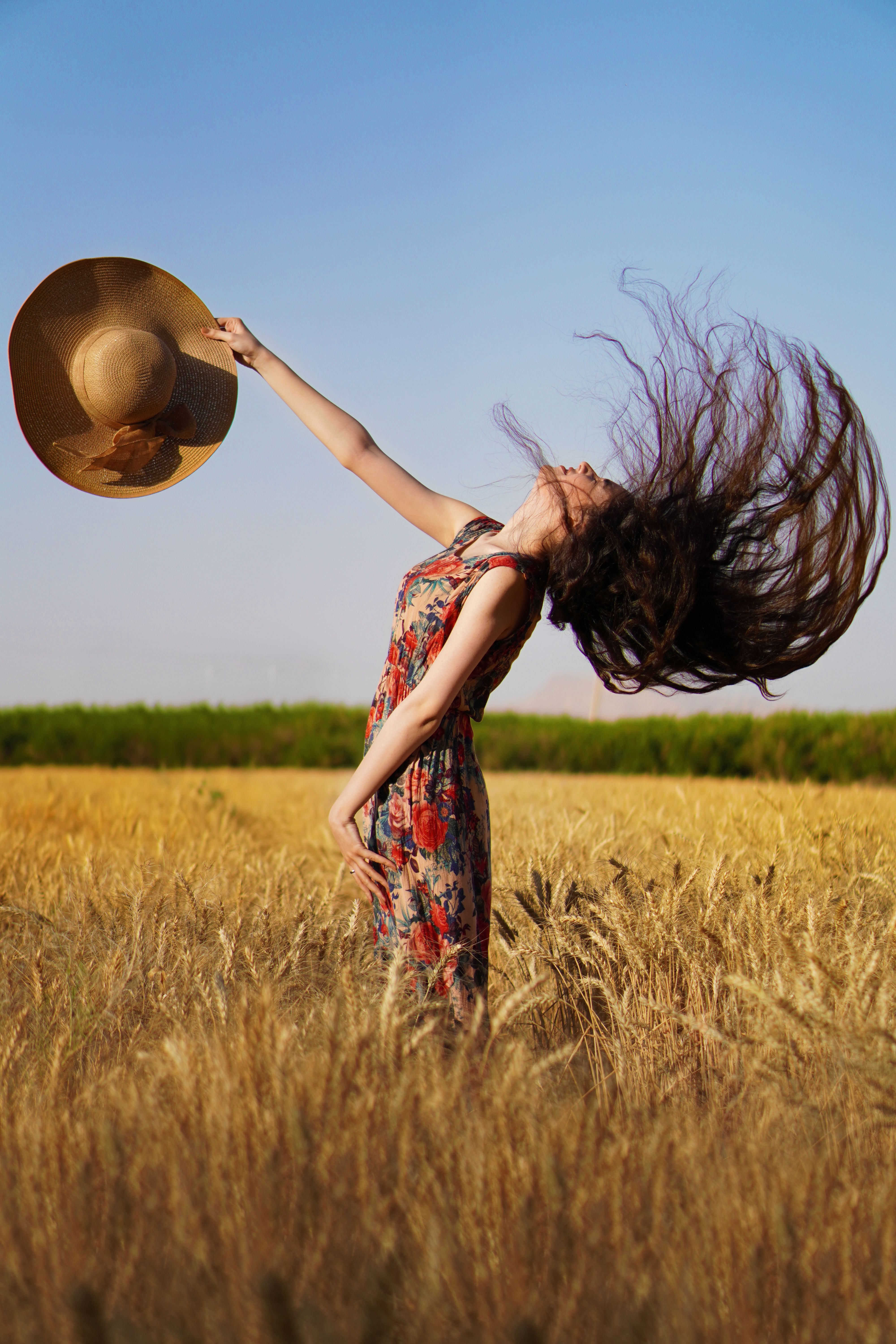 A woman in a floral dress flips her hair in a sunny wheat field, creating a dynamic, carefree pose.