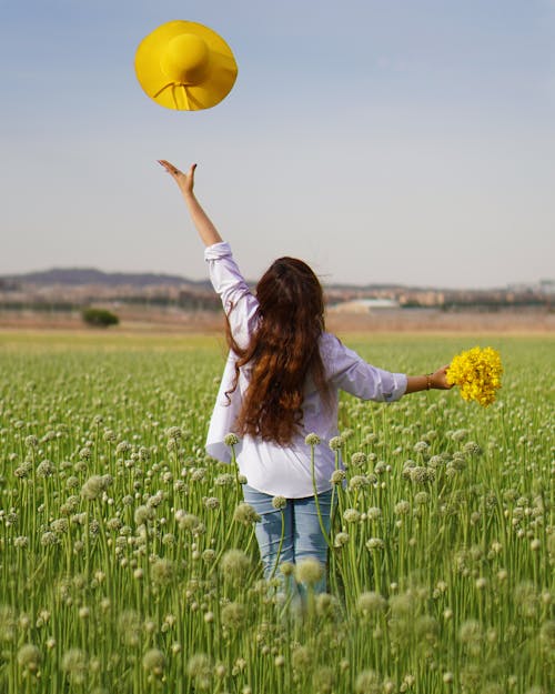 A Person Holding a Bunch of Yellow Flowers Tossing a Straw Hat in the Air