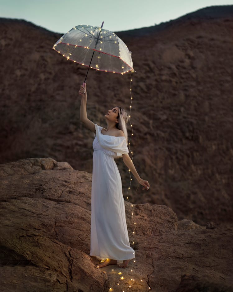 A Woman In White Dress Holding A Translucent Umbrella With String Lights