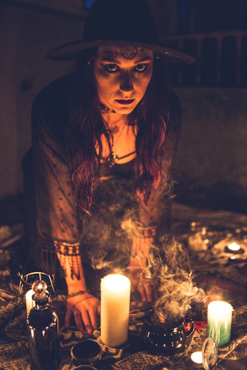 Spooky sorceress among candles in dark