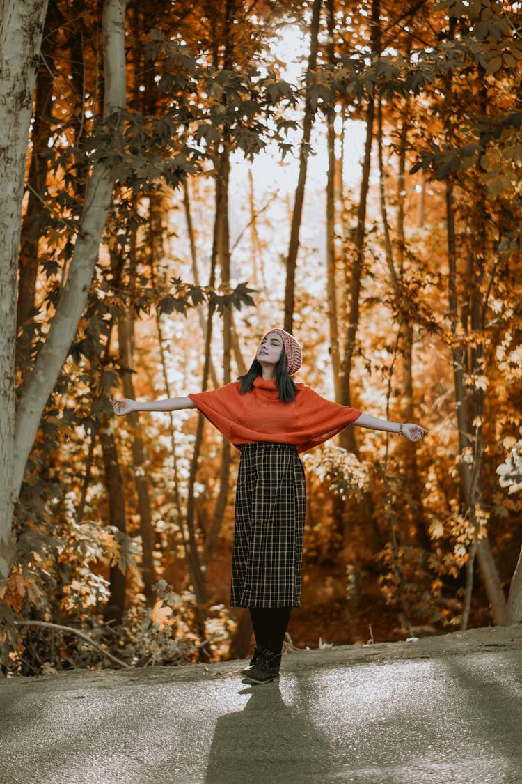 A Woman In Red Knit Cap Standing On The Road Side With Arms Raised On Sides