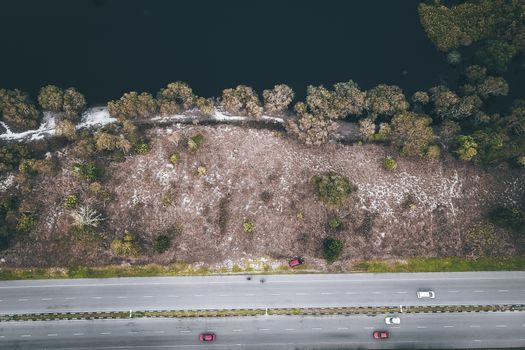 Drone view of tiny automobiles riding on paved roads by dark blue reservoir and green trees