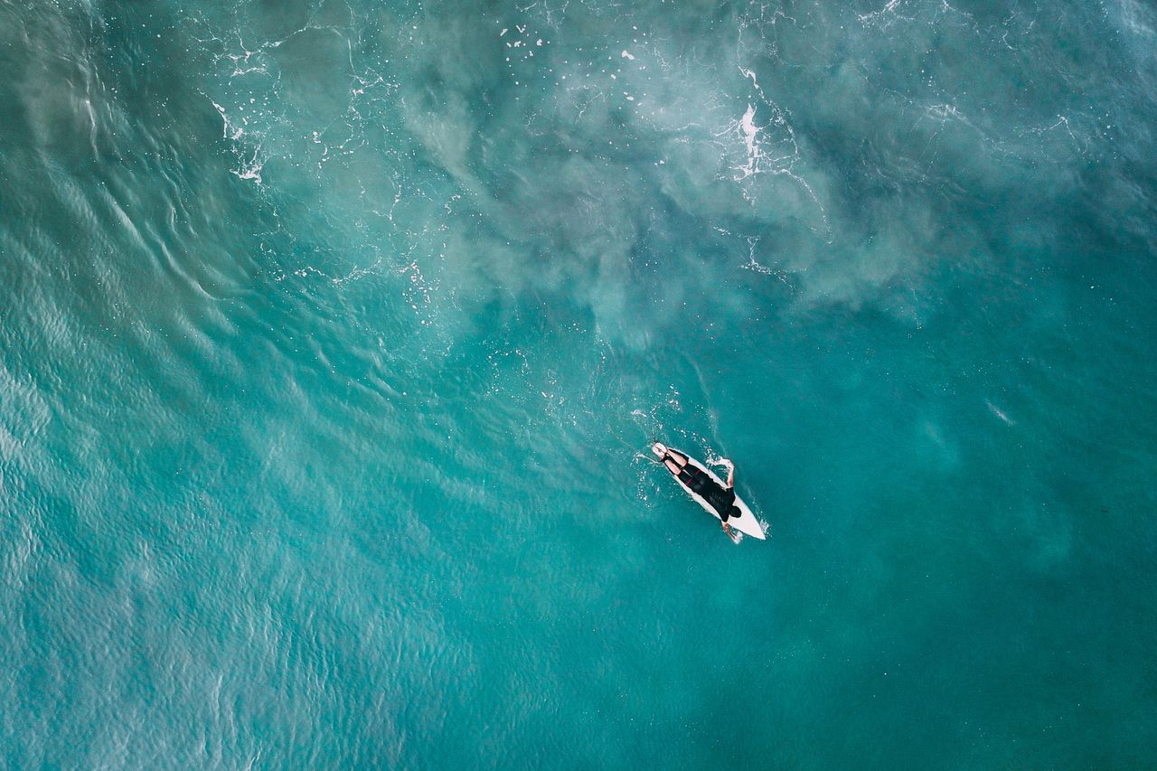 drone view of faceless sports man on white longboard surfing in vibran