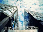 从低角度仰望现代摩天大楼，其玻璃外墙在城市环境中映照着云层