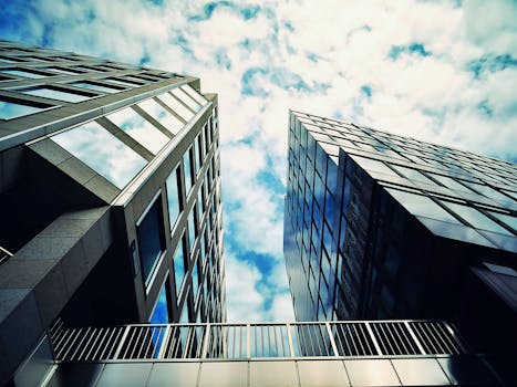 从低角度仰望现代摩天大楼，其玻璃外墙在城市环境中映照着云层