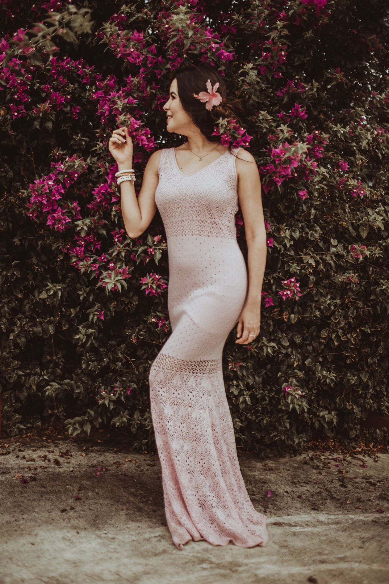 Woman in a light pink crochet lace maxi dress standing before a bougainvillea wall