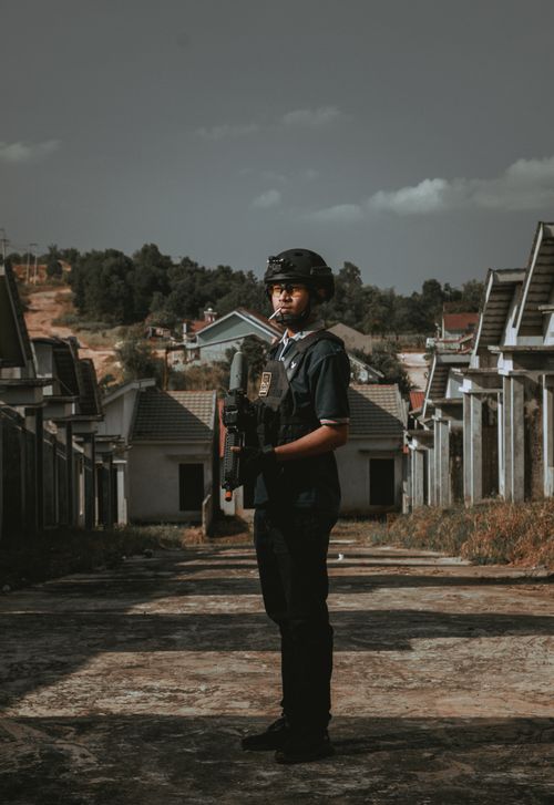 Free Man in tactical gear holding rifle in deserted area with houses in background. Stock Photo