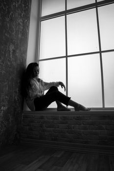 一个体贴的女人坐在窗台上，宁静的黑白图像将她定格