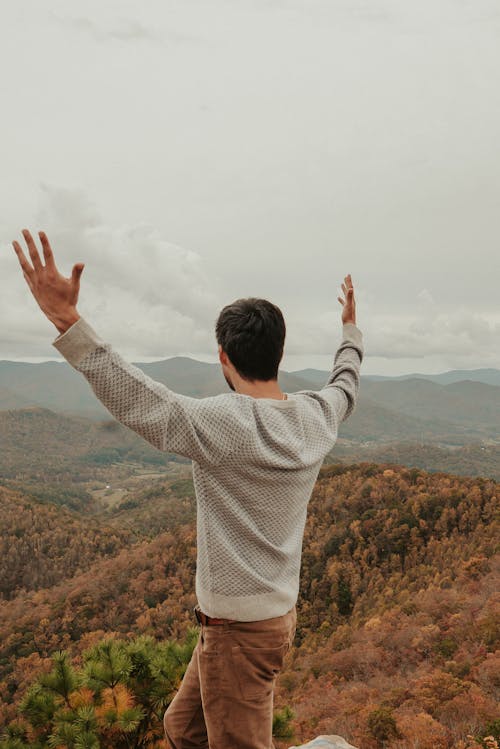 Free Anonymous man recreating on mountain top with outstretched arms and admiring landscape Stock Photo