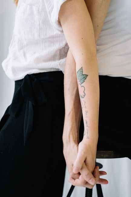A close-up image of a couple holding hands, showcasing a tattooed arm and a sense of connection.